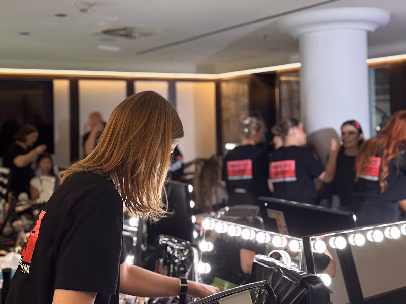 Person mit Famous Face Academy T-Shirt vor einem Schminkspiegel