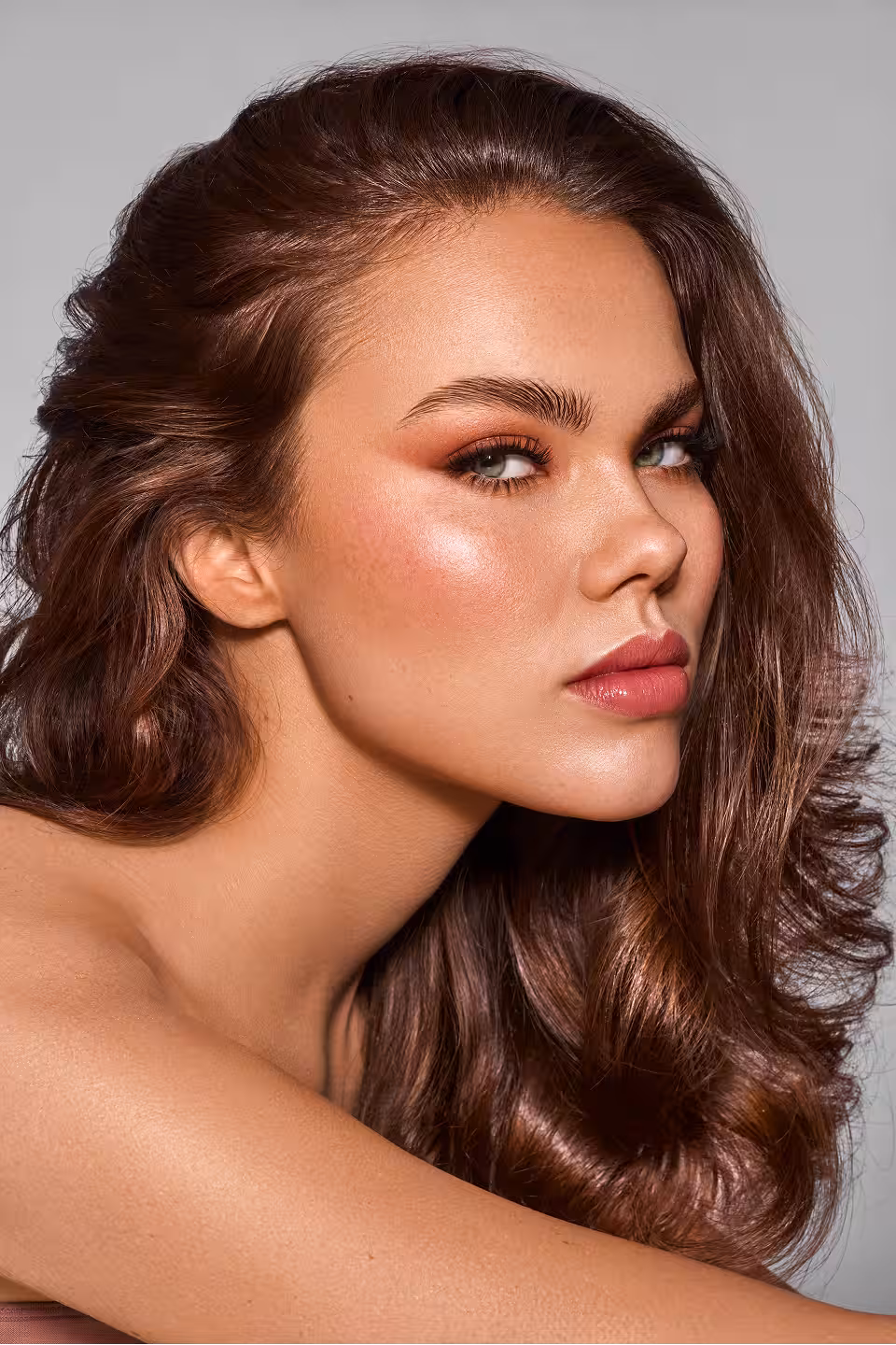 Nahaufnahme eines Models mit bronziertem Make-up und welligem, glänzendem Haar.